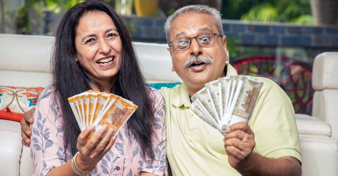 1541973346 Happy mature senior Indian couple holding money rupee notes in hand while sitting at home. Savings and banking concept
